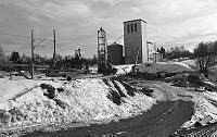 Fra omleggingen av E18 gjennom Askim februar 1979. Man driver og graver seg under jernbanesporet der jernbanen skal gå i en bro over veien. Vi ser Askim Mølle og 01kornsiloen i bakgrunnen.